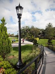 حديقة خلابة تضم أعمدة إنارة فيبر جلاس ديكورية باللون الأسود وسط مساحات خضراء شاسعة ومسارات متعرجة، حيث يتنزه الزوار تحت سماء غائمة جزئياً، مما يبرز جمال أعمدة إنارة الحدائق في إضفاء أجواء هادئة وآمنة.