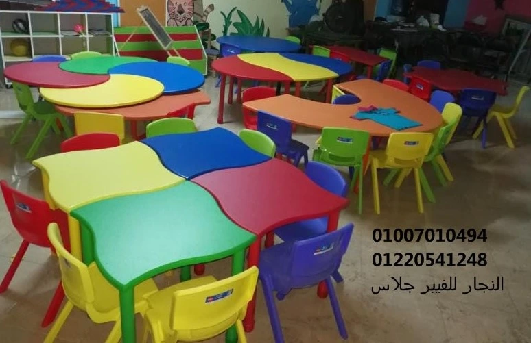 فصل دراسي ملون يضم طاولات وكراسي فيبر جلاس متداخلة بألوان مبهجة (أحمر، أصفر، أخضر، أزرق)، مصممة بجودة عالية لتوفير بيئة تعليمية مريحة وعصرية للحضانات والمدارس.