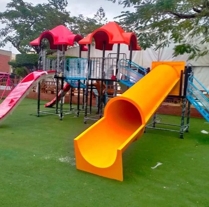 مجمع ألعاب أطفال فيبر جلاس يضم هياكل بأسقف حمراء وزحاليق فيبر جلاس باللونين الأزرق والأحمر، مع زحليقة أنبوبية فيبر جلاس صفراء مميزة على نجيل صناعي، مثالية لتجهيز ملاهي وحدائق ترفيهية ممتعة.