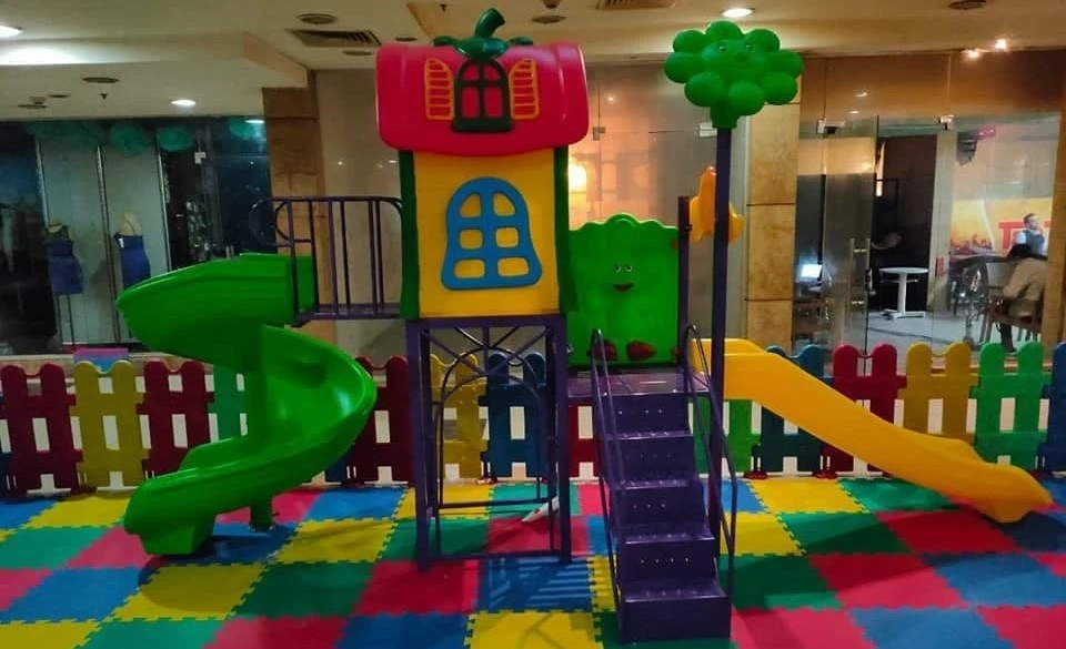 "منطقة ألعاب أطفال مغلقة تضم زحليقة فيبر جلاس على شكل كوخ بسقف أحمر محاطة بسياج حماية ملون لتجهيز كيدز اريا وحضانات"