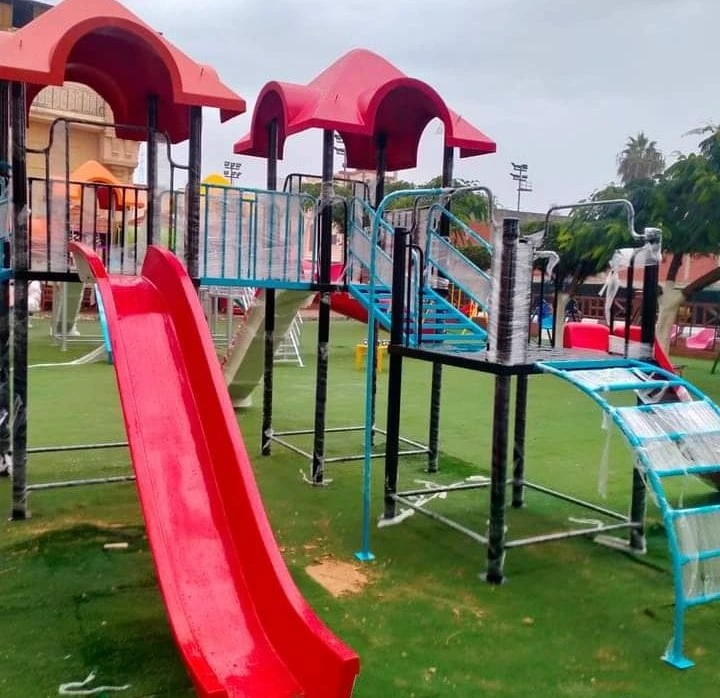 مجمع ألعاب أطفال فيبر جلاس بتصميم مبهج يضم زحاليق فيبر جلاس حمراء وهياكل تسلق زرقاء مع أسطح منحنية فوق مسطح أخضر، مثالي لتجهيز حضانات وملاهي خارجية بأفضل خامات الفيبر جلاس.