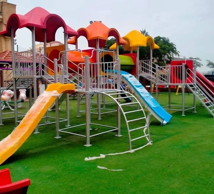 مجموعة ألعاب أطفال فيبر جلاس ملونة على مسطح أخضر، تضم زحاليق فيبر جلاس وأنفاق للأطفال بألوان الأحمر والأصفر والأزرق، مصممة لتجهيز ملاهي وحضانات بأعلى جودة.