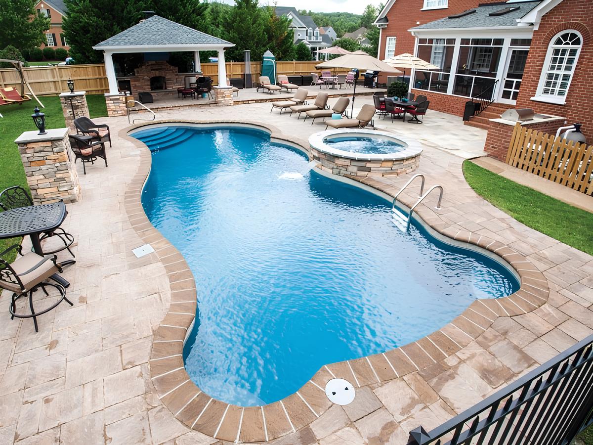 حمام سباحة فيبر جلاس بتصميم كيدني فاخر مع جاكوزي متصل، محاط بأرضيات حجرية ومنطقة جلوس مغطاة توفر أقصى درجات الراحة والرفاهية في الحدائق المنزلية.