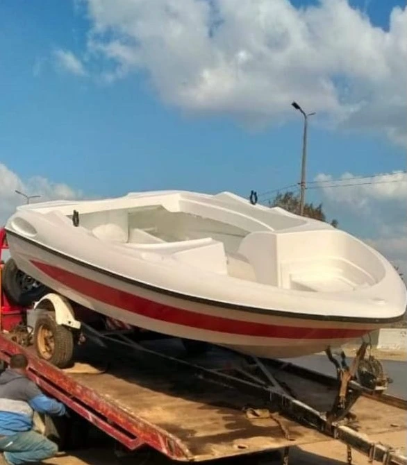 قارب سريع (لانش) فيبر جلاس باللونين الأبيض والأحمر محمول على مقطورة يتم تحميله على شاحنة، مصنوع من أجود خامات الفيبر جلاس لضمان القوة والمتانة، مثالي للاستخدام في الألعاب المائية والرحلات البحرية.