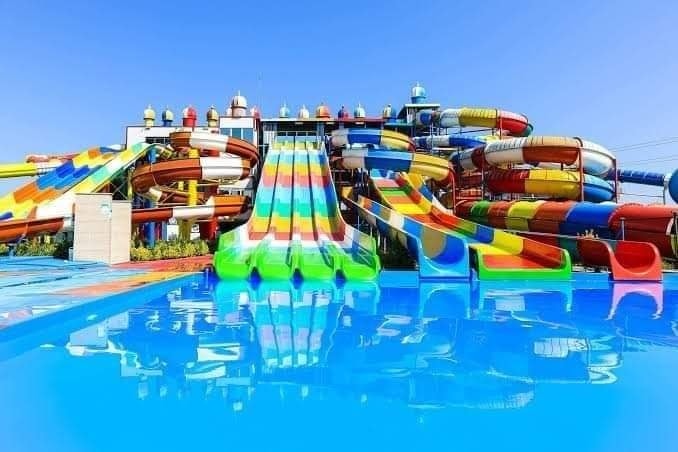 زحاليق مائية فيبر جلاس ملونة بتصيميمات لولبية ومنحنية تصب في حمام سباحة أزرق صافٍ، توفر أقصى درجات الإثارة والمرح ضمن تجهيزات أكوا بارك فيبر جلاس المتكاملة للملاهي المائية.