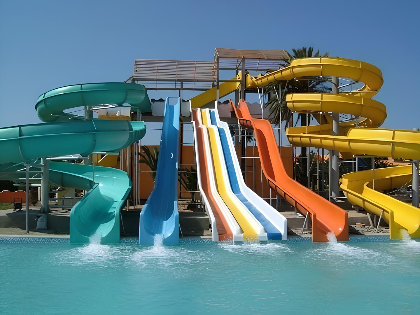 ألعاب مائية فيبر جلاس ملونة تضم مجموعة من الزحاليق المائية بألوان الأخضر والأزرق والأبيض والبرتقالي والأصفر، تنتهي في حمام سباحة مشمس، مما يوفر أفضل تجهيزات أكوا بارك فيبر جلاس للاستمتاع بأجواء ترفيهية مرحة.