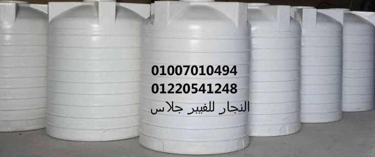 صف من خزانات مياه فيبر جلاس كبيرة الحجم باللون الأبيض، مثبتة على أرضية خرسانية في موقع صناعي، وتظهر عليها أرقام التواصل وبيانات المصنع باللغة العربية، مصنعة من أجود خامات الفيبر جلاس لضمان القوة والمتانة في تخزين المياه والكيماويات.