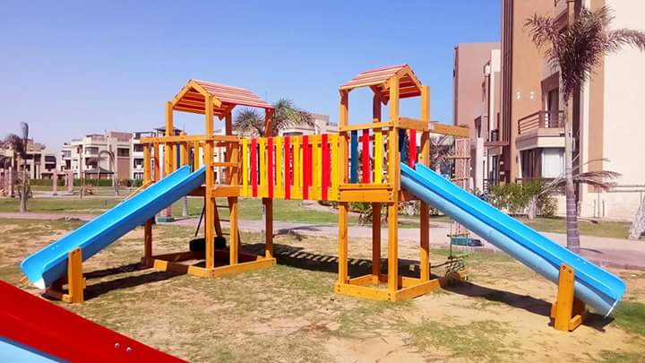 مجمع ألعاب خشبية ملون للحدائق يضم برجين خشبيين مع زحليقتين فيبر جلاس باللون الأزرق، يتميز بتصاميم جذابة باللونين الأحمر والأصفر، مصمم بأعلى معايير الأمان لتجهيز مناطق ألعاب الأطفال في المجمعات السكنية.