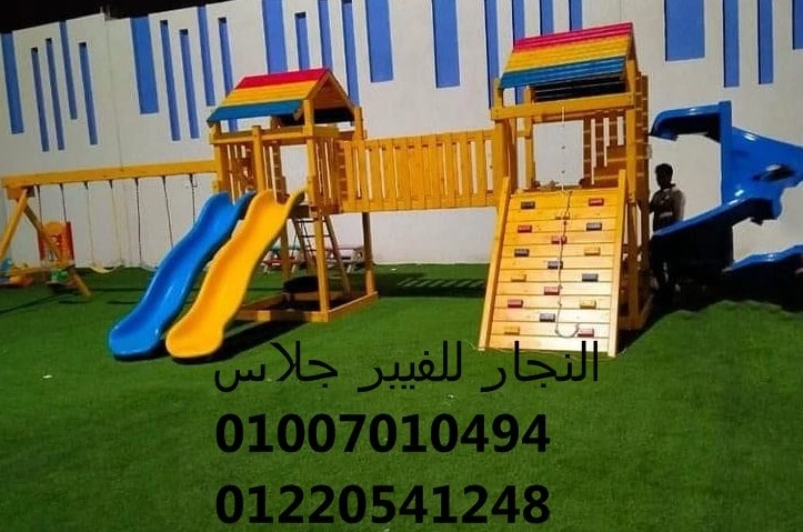 مجمع ألعاب خشبية ملون للحدائق يضم زحاليق فيبر جلاس، أرجوحة، وجدار تسلق، مثبت على نجيل صناعي عالي الجودة لتوفير منطقة ترفيهية آمنة للأطفال في المدارس والنوادي مع أرقام التواصل للتجهيزات.