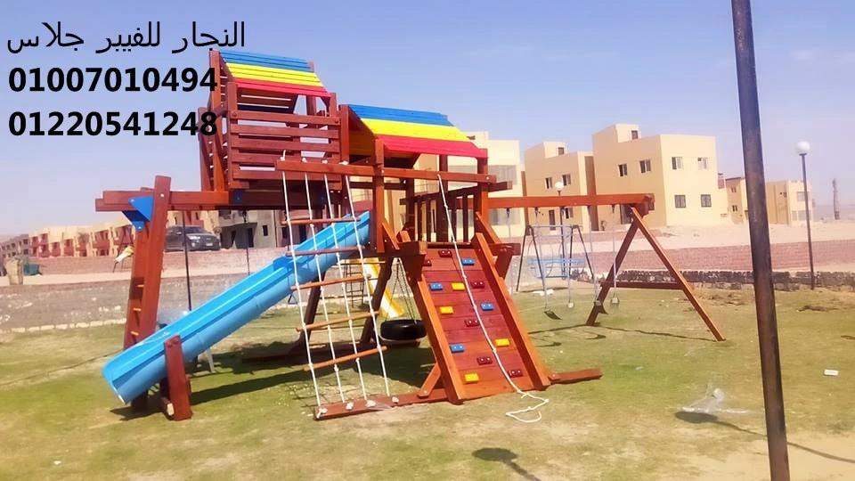 مجمع ألعاب خشبية ملون للحدائق يضم زحليقة فيبر جلاس وجدار تسلق وأراجيح متينة، مثبت على مساحة خضراء واسعة لتجهيز مناطق ألعاب الأطفال في الفلل والمجمعات السكنية بأعلى معايير الأمان.