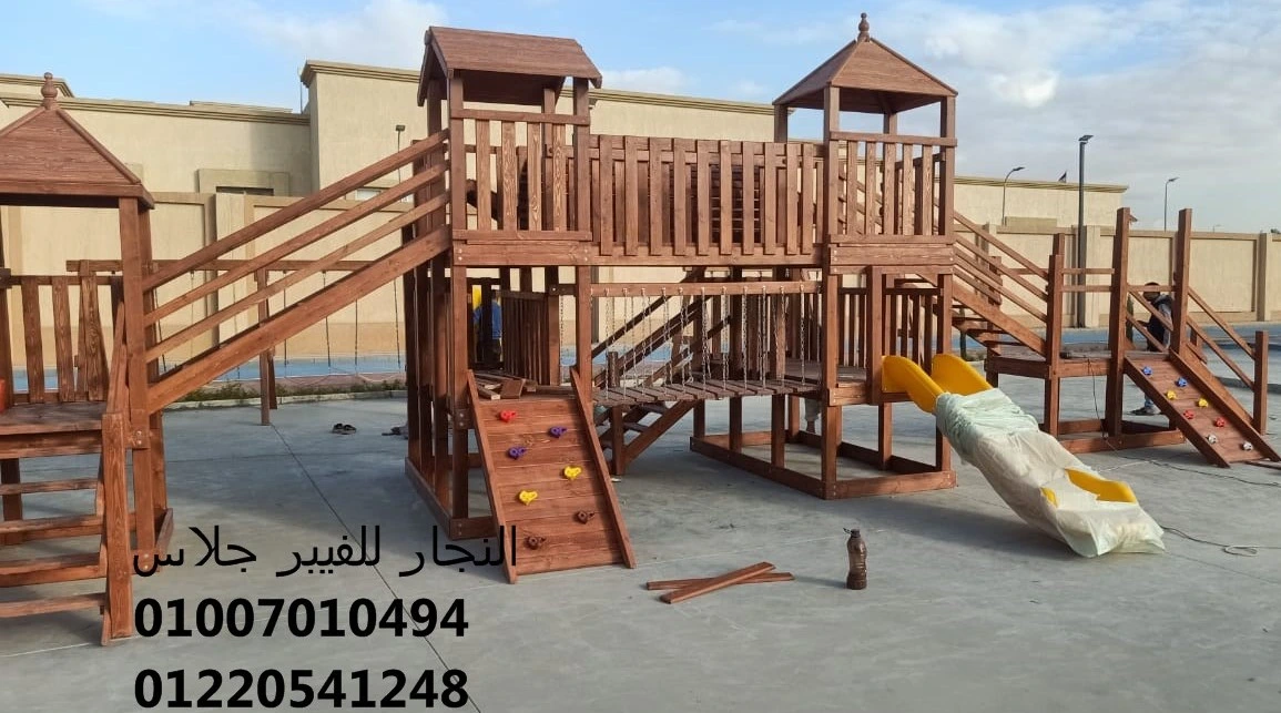 مجمع ألعاب خشبية خارجي مجهز بزحاليق فيبر جلاس صفراء زاهية، يضم جدران تسلق وجسور حبال متينة، مصمم بأعلى معايير الأمان ليناسب الحدائق والمدارس والمناطق الترفيهية.