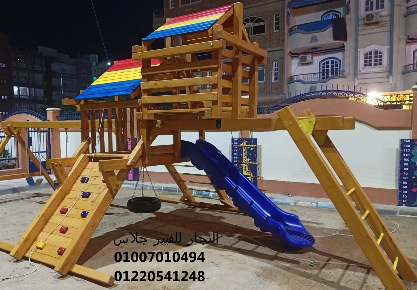 مجمع ألعاب خشبية للحدائق بتصميم ليلي مبهج، يضم زحليقة فيبر جلاس زرقاء، جدار تسلق، وأرجوحة إطارات، مع أسقف ملونة وإضاءة ساطعة لتوفير منطقة ترفيهية آمنة وممتعة للأطفال.