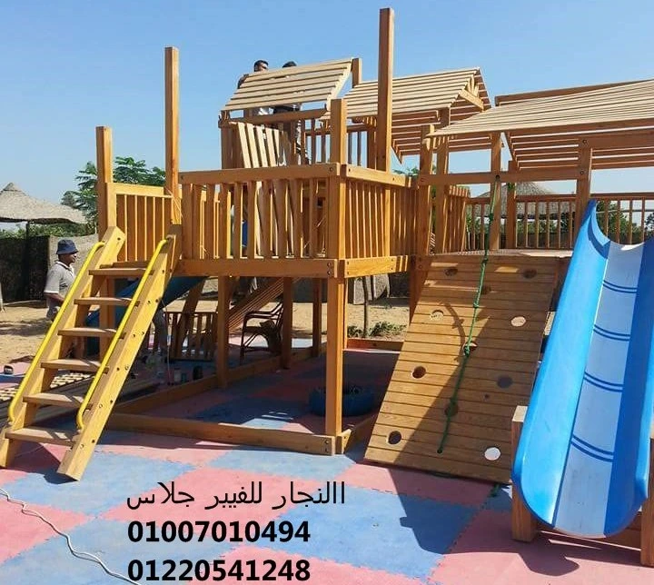 مجمع ألعاب خشبية للحدائق يضم سلالم وجدار تسلق مع زحليقة فيبر جلاس زرقاء، مثبت على أرضية مطاطية ملونة (Safe Rubber) لضمان أمان الأطفال في المناطق الترفيهية المفتوحة.