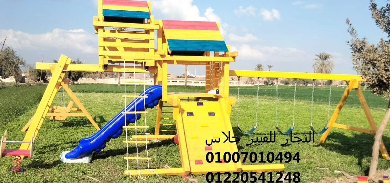 مجمع ألعاب خشبية ملون للحدائق يضم زحليقة فيبر جلاس زرقاء، جدار تسلق، وأراجيح متينة مثبتة على نجيل طبيعي، مصمم لتوفير منطقة ترفيهية آمنة ومقاومة للعوامل الجوية مع أرقام التواصل للتجهيزات.